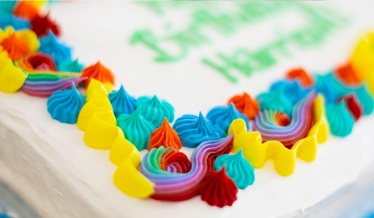 Close-up of a quarter-sheet ice cream cake from Over The Top Ice Cream, featuring rainbow decorations on a white birthday cake.