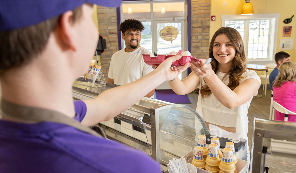 An Over The Top Ice Cream scooper serving a flight of ice cream in a pink carton to a couple.