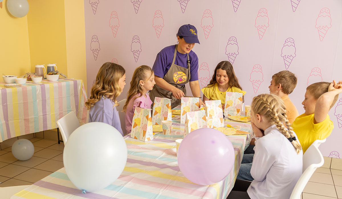 An Over The Top Ice Cream scooper serves cake to birthday party guests in the party room.