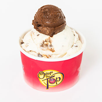 A single scoop of Over The Top Ice Cream in a branded cup, featuring one of their signature topper scoops.